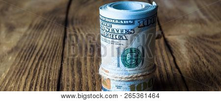 A Roll Of Dollars Stands On A Wooden Table.