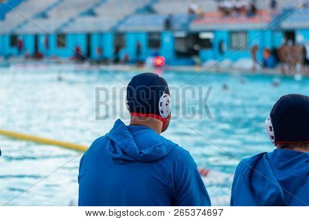 Two Water Polo Reserved Players Observing The Game  Sitting On A Bench. Background Out Of Focus. Cop