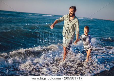 Happy Father And Son, Man & Boy Child, Running And Having Fun In The Sand And Waves Of A Sunny Beach