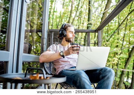 Poortrait Of A Handsome Man Working With Laptop On The Balcony Of The House In The Beautiful Green F
