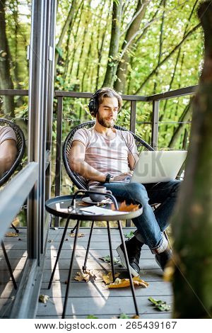 Poortrait Of A Handsome Man Working With Laptop On The Balcony Of The House In The Beautiful Green F
