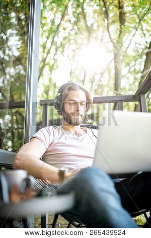 Poortrait Of A Handsome Man Working With Laptop On The Balcony Of The House In The Beautiful Green F