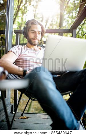 Poortrait Of A Handsome Man Working With Laptop On The Balcony Of The House In The Beautiful Green F