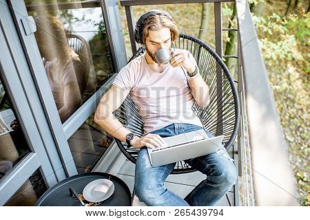 Poortrait Of A Handsome Man Working With Laptop On The Balcony Of The House In The Beautiful Green F