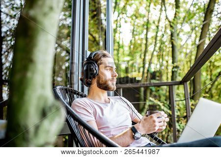 Poortrait Of A Handsome Man Working With Laptop And Headphones On The Balcony Of The House In The Be