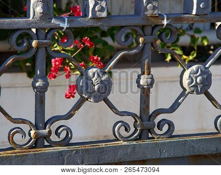 Closeup Setails Of Ornate Wrought Iron Elements  Metal Gate With Flowers In The Background