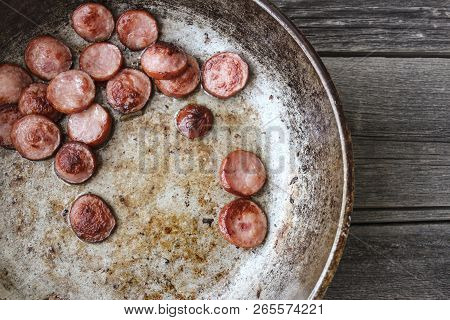 Frying Pan With Fried Pieces Of Sausages On An Old Wooden Table