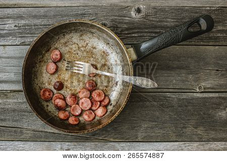 Frying Pan With Fried Pieces Of Sausages On An Old Wooden Table