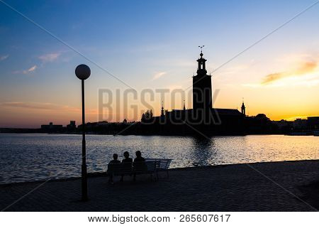 Silhouette Of Women Sitting On Bench At Promenade Quay Bank Of Lake Malaren Looking At Stockholm Cit