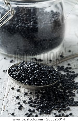 Heap Of Black Organic Beluga Lentils In Metal Spoon With Black Beluga Lentils In Storage Jar On Whit