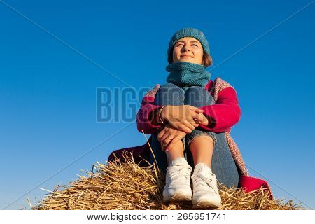 Young Attractive Lady In Blue Knitting Hat And Pink Coat Sitting On Haystack. Smiling Beautiful Hips
