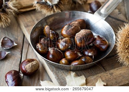 Roasted Chestnuts In Cast Iron Grilling Pan Over Rustic Wooden Board Background, Selective Focus, Ro