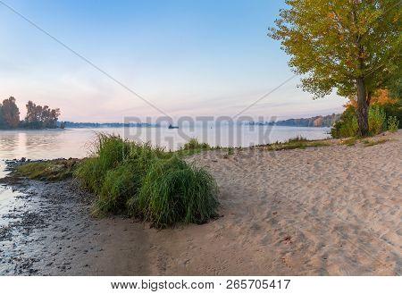 Section Of The Plain River With Sandy Bank And Trees With Autumn Leaves On A Foreground, Fog Over Wa