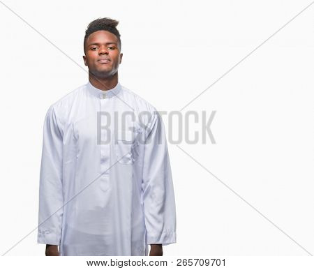 Young arabic african man wearing traditional djellaba over isolated background with serious expression on face. Simple and natural looking at the camera.