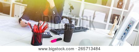 Beautiful Young Girl Is Looking Through Documents, Sitting In The Office At The Table.