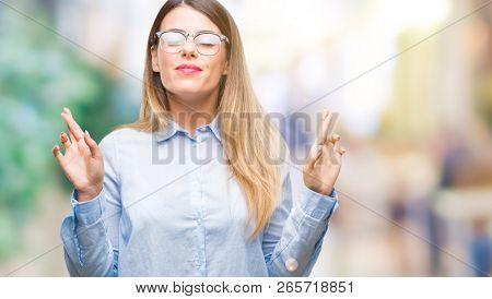 Young beautiful business woman wearing glasses over isolated background smiling crossing fingers with hope and eyes closed. Luck and superstitious concept.