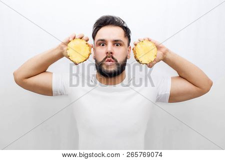 Really Amazed Young Man Stand And Look On Camera. He Coveres Ears With Two Halfs Of One Pineapple. G