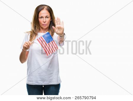 Middle age hispanic woman holding flag of United States of America over isolated background with open hand doing stop sign with serious and confident expression, defense gesture