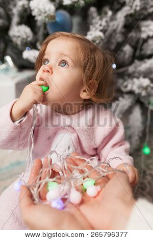 A Little Girl Is Playing With A Garland With A New Year Tree. Danger. Disobedient Child. Good New Ye