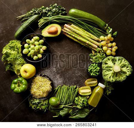 Round green healthy food composition with avocado, broccoli, apple, smoothie, cucomber, asparagus, kiwi, bean. Placed on dark background. Top view with copy space in the middle.