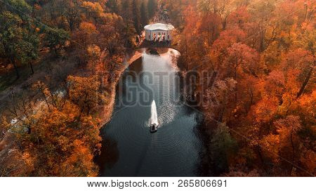 Aerial View Of The Beautiful Autumn Orange Landscape Park With A Pond And A Fountain In The Center, 