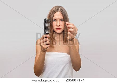 Worried Young Woman Stands And Shows Falled Hair And Comb. She Is Upset And Unsatisfied. White Towel