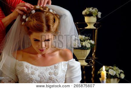 Pick up wedding dress and veil in shop. Woman in wedding robes and bobbinet dreams of holiday night. Candle stands on table decorated flowers.
