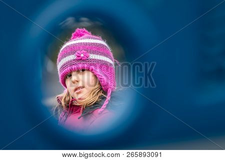 Young Girl In A Pink Hat Peeking Through The Hole Among The Various Hideouts In The Playground