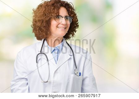 Middle ager senior doctor woman over isolated background looking away to side with smile on face, natural expression. Laughing confident.