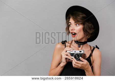 Photo of camerawoman 20s wearing black dress and hat holding retro camera isolated over gray background