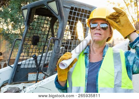 Female Worker Holding Technical Blueprints Near Small Bulldozer At Constrcution Site