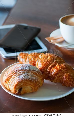 Fresh Croissants, A Cup Of Cappuccino And Digital Gadjets On A Working Table. Coffee Break Or Busine
