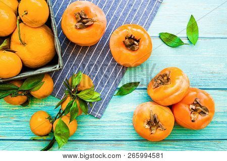 Healthy Diet Concept. Fresh Ripe Persimmons And Tangerines On Blue Wooden Background Top View Flt La