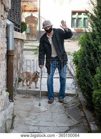 Senior Man In Protective Mask With A Cane Walking With A Dog