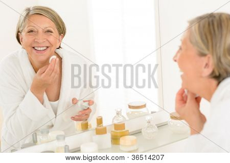 Starší žena usmívající se čištění obličeje make-up odstranění koupelna zrcadlový odraz