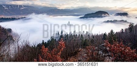 amazing panorama of Lake Bled Blejsko Jezero on a foggy morning with the Pilgrimage Church of the Assumption of Maria on a small island and Bled Castle and Julian Alps in backgroud
