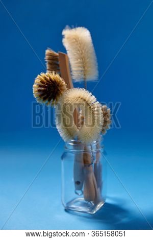 cleaning stuff, sustainability and eco living concept - different brushes with natural bristle and wooden handles in glass jar on blue background