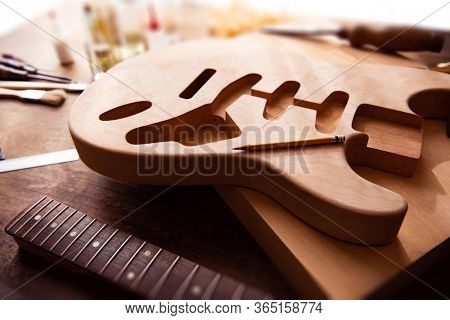 Electric guitar making. Guitar work shop. Unfinished solidbody electric guitar body on work bench. Focus is on pencil. Shallow depth of field.  