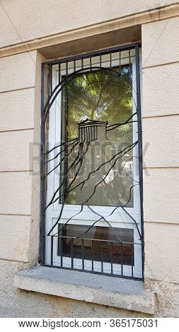Ornate Metal Grating Protected White Window With Blurry Reflection In Window Glass. Details Of Class