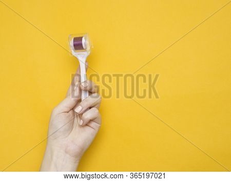 Mezoroller, Dermaroller, Mesotherapy Skin Tool In A Woman's Hand On A Yellow Background. Copy Space.