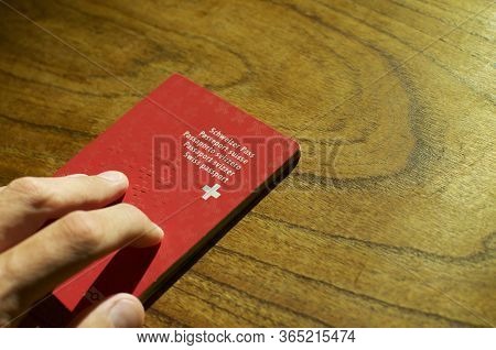 Male Hand Putting A Swiss Passport On A Wooden Table