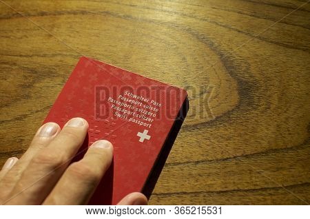 Male Hand Putting A Swiss Passport N A Wooden Table