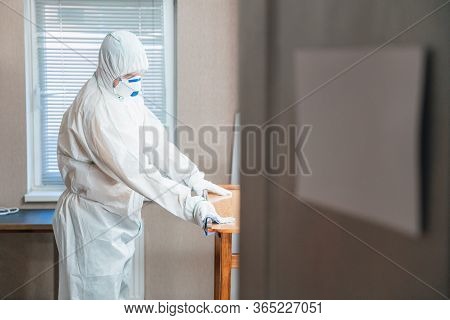 Coronavirus Pandemic. A Disinfector In A Protective Suit And Mask Sprays Disinfectants In House Or O
