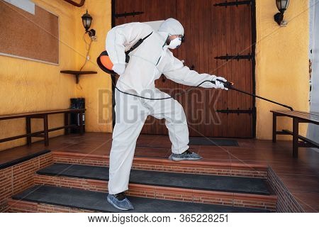 Coronavirus Pandemic. A Disinfector In A Protective Suit And Mask Sprays Disinfectants In House Or O