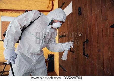 Coronavirus Pandemic. A Disinfector In A Protective Suit And Mask Sprays Disinfectants In House Or O