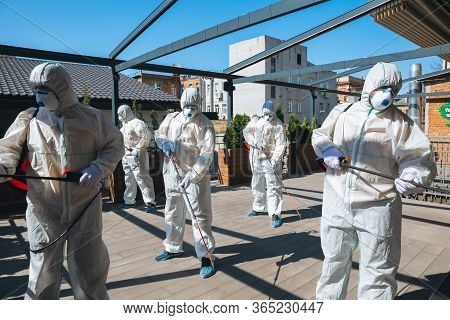 Coronavirus Pandemic. A Disinfectors In A Protective Suit And Mask Spray Disinfectants In House Or O