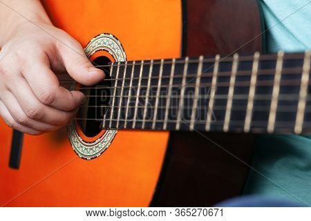 Male Hand Plays Acoustic Guitar Strings. Learning To Play A Musical Instrument Orange Color Close-up
