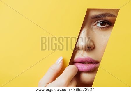Woman With Pink Lips Looking At Camera Across Quadrangular Hole And Touching Yellow Paper