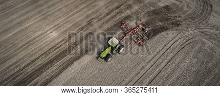 Aerial View Of A Clean Field In Which The Tractor Makes Vertical Tillage. Red Tillage Equipment And 