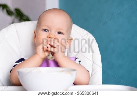 Baby Food. Little Caucasian Child With Spoon In His Mouth Got Dirty In Porridge On Highchair. Newbor